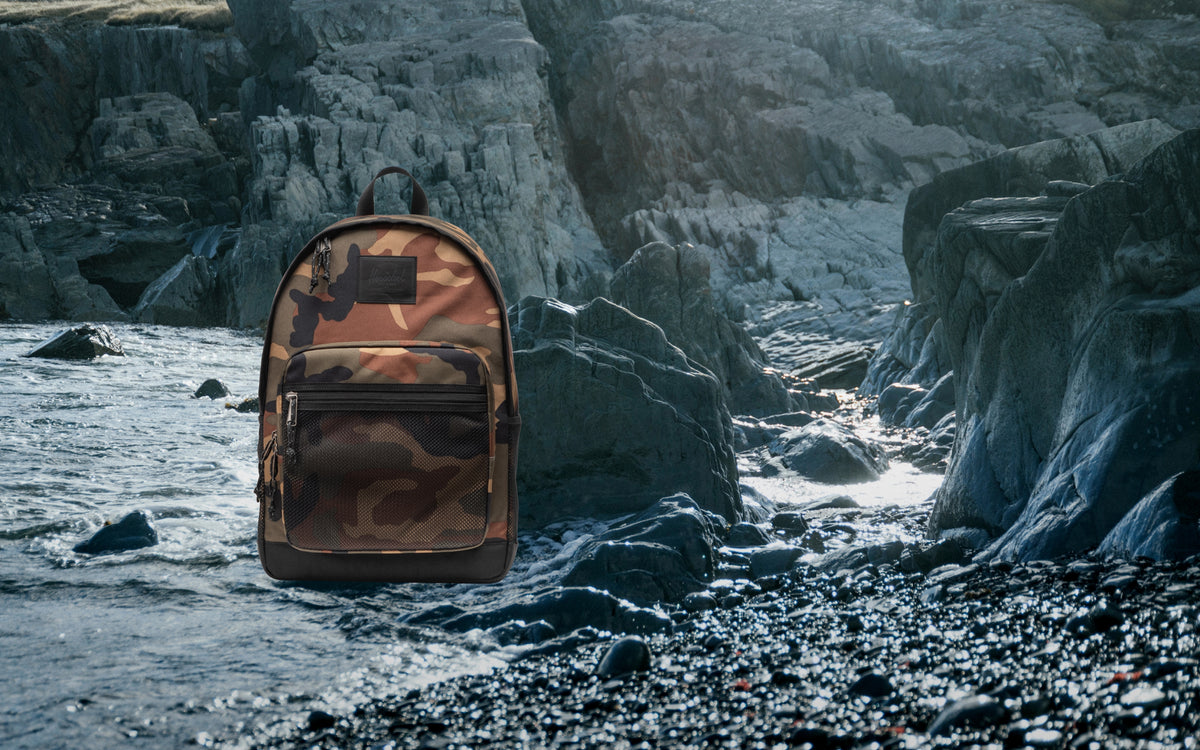 Herschel Supply Co. Kaine Backpack in Woodland Camo/Black shown from the front, highlighting its multi-pocket design and durable straps.