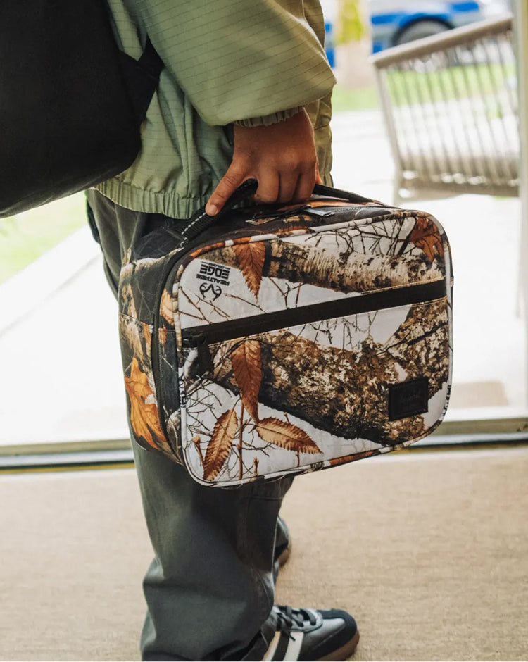 Herschel Supply Co. Realtree Pop Quiz Lunch Box in Realtree Edge Camo White/Black with insulated main compartment and front pocket.